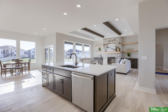 kitchen featuring light wood finished floors, light countertops, a sink, a stone fireplace, and dishwasher