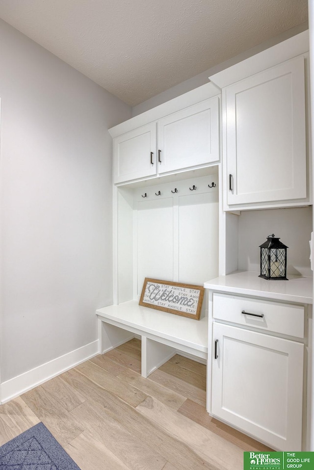 mudroom featuring light wood-style flooring, baseboards, and a textured ceiling