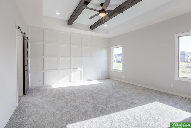 spare room with a barn door, baseboards, ceiling fan, carpet, and beam ceiling