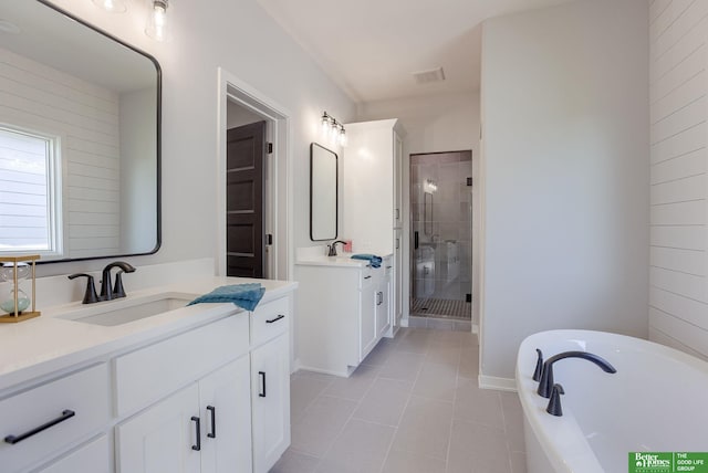 full bath with a stall shower, a sink, tile patterned flooring, a freestanding tub, and two vanities