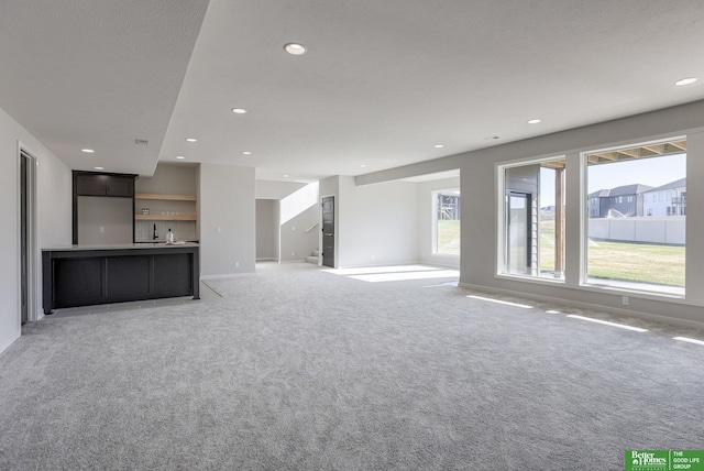 unfurnished living room featuring recessed lighting, stairs, baseboards, and light colored carpet