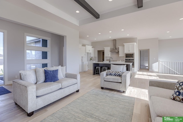 living room featuring light wood-style floors, recessed lighting, beam ceiling, and baseboards