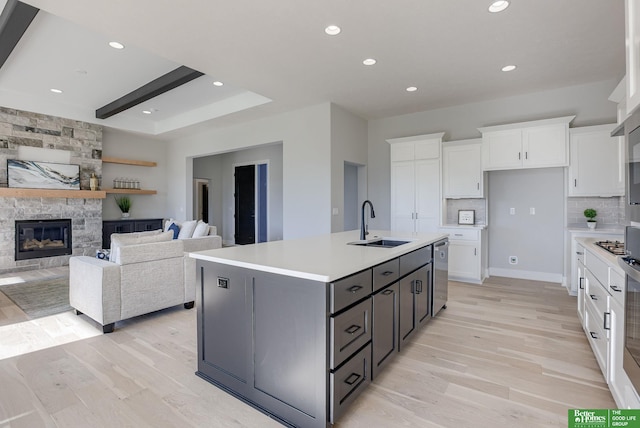 kitchen featuring a stone fireplace, stainless steel appliances, a sink, white cabinetry, and light wood finished floors