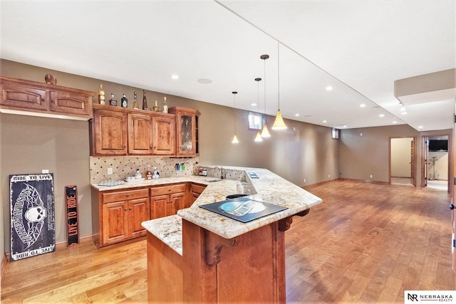 kitchen featuring brown cabinets, light wood finished floors, glass insert cabinets, a peninsula, and a kitchen breakfast bar