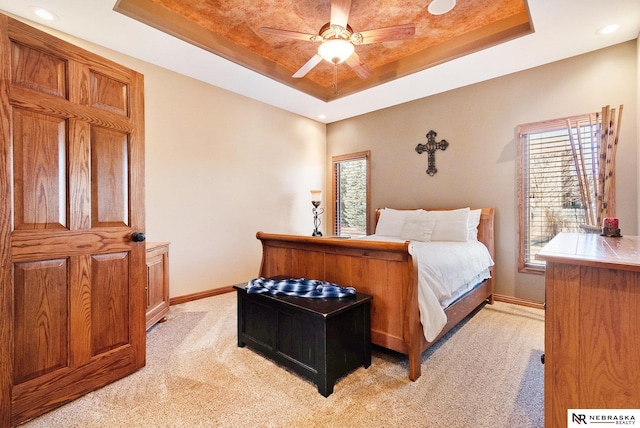 bedroom featuring baseboards, a raised ceiling, a ceiling fan, and light colored carpet