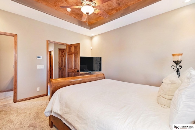 carpeted bedroom with baseboards, a tray ceiling, and ceiling fan