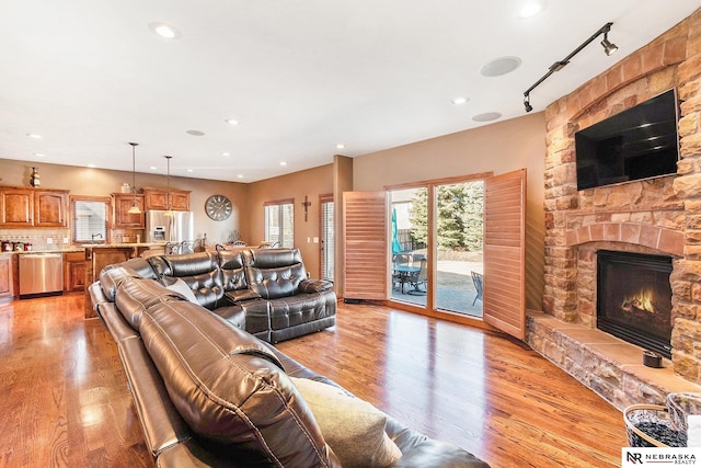 living room with recessed lighting, rail lighting, light wood-style flooring, and a stone fireplace