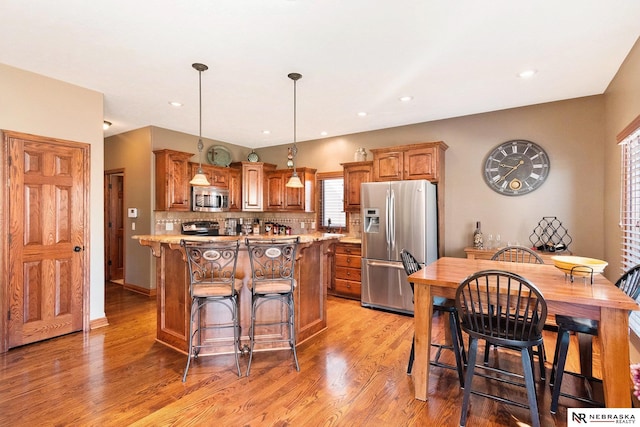 kitchen with brown cabinets, stainless steel appliances, backsplash, light wood-style floors, and a kitchen island