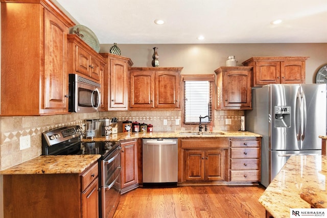 kitchen featuring light stone counters, light wood-style flooring, stainless steel appliances, a sink, and brown cabinetry