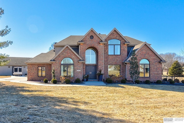 view of front facade featuring brick siding, a front lawn, and roof with shingles