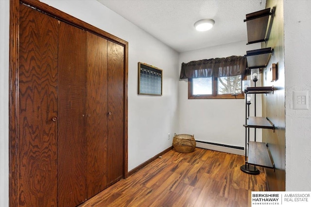 interior space with a baseboard radiator, a closet, a textured ceiling, wood finished floors, and baseboards