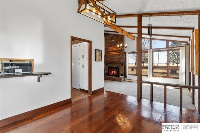 unfurnished living room with baseboards, wood-type flooring, beamed ceiling, an inviting chandelier, and a fireplace