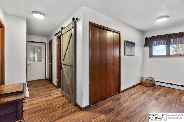 corridor featuring wood finished floors, a textured ceiling, baseboard heating, and a barn door