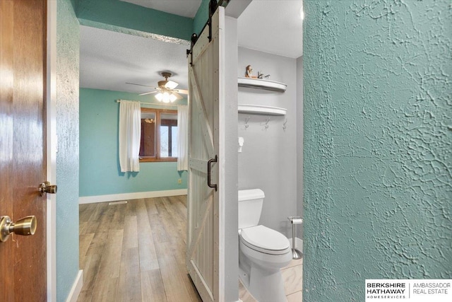 bathroom featuring baseboards, a ceiling fan, toilet, wood finished floors, and a textured ceiling