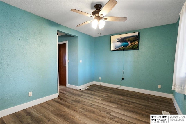 unfurnished room featuring dark wood-style flooring, a ceiling fan, and baseboards