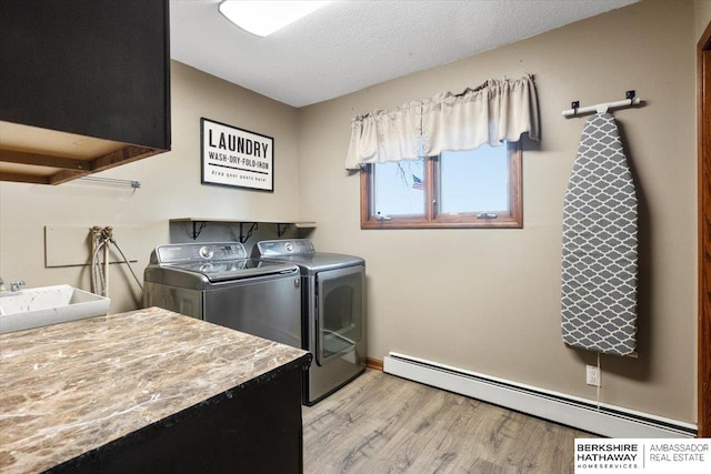 laundry room with a baseboard heating unit, a sink, light wood-style floors, cabinet space, and washer and clothes dryer