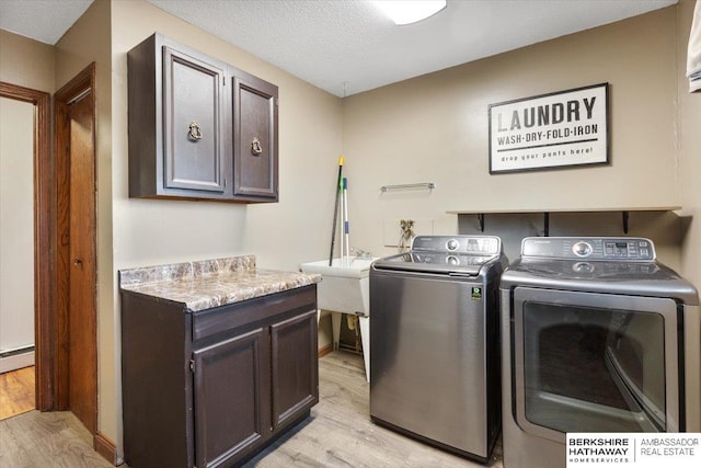 laundry room with washing machine and clothes dryer, cabinet space, light wood-style floors, a sink, and a textured ceiling