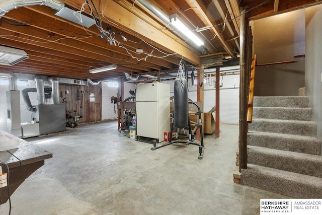 unfinished below grade area with heating unit, stairway, and freestanding refrigerator