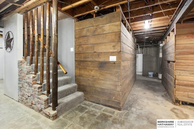 unfinished basement with water heater, wooden walls, and stairs