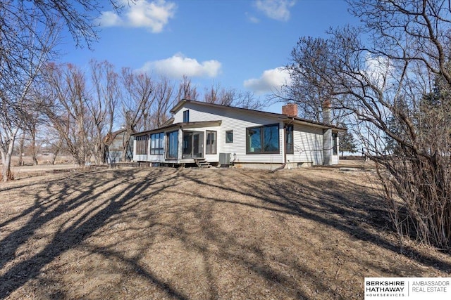 rear view of property featuring a sunroom, a chimney, and central AC