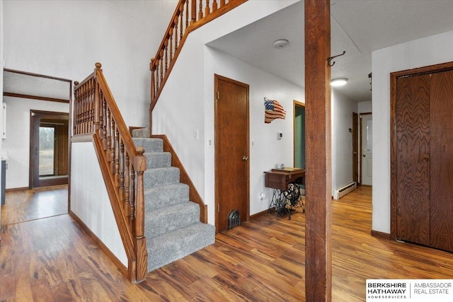 staircase with a baseboard heating unit, wood finished floors, and baseboards