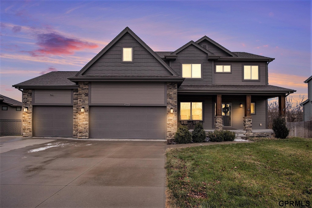 view of front of house with an attached garage, driveway, a porch, and a front yard