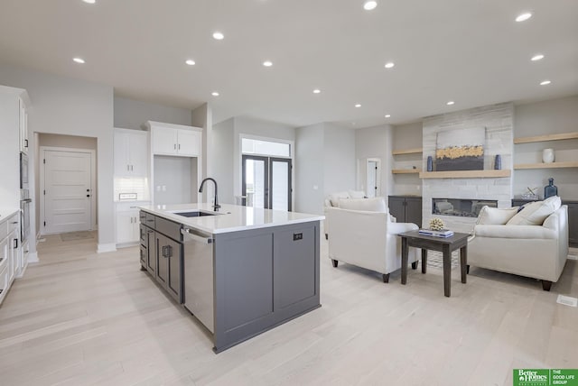 kitchen featuring a stone fireplace, a sink, white cabinets, open floor plan, and appliances with stainless steel finishes