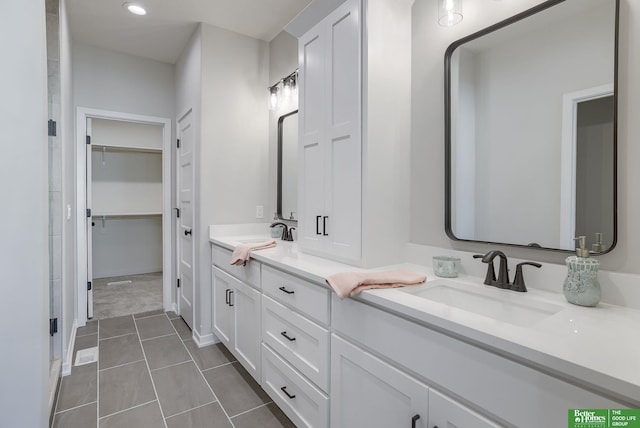 bathroom with double vanity, a walk in closet, a sink, and tile patterned floors