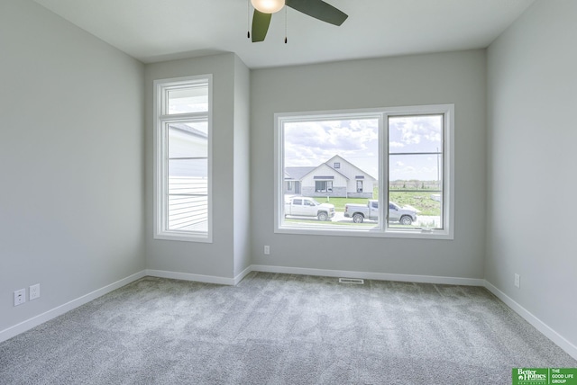 carpeted spare room featuring visible vents, ceiling fan, and baseboards