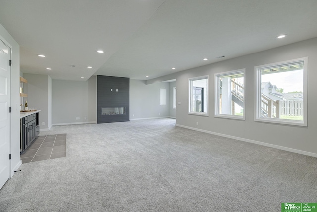 unfurnished living room with recessed lighting, a large fireplace, light colored carpet, baseboards, and a bar