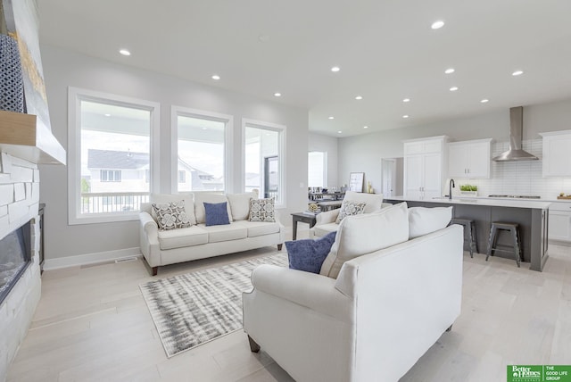 living room with baseboards, a stone fireplace, light wood-style flooring, and recessed lighting