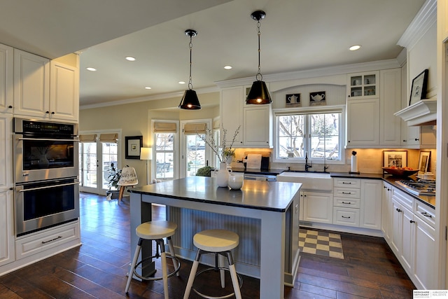 kitchen with dark wood-style flooring, a sink, appliances with stainless steel finishes, dark countertops, and crown molding