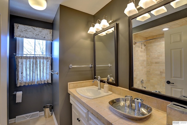 bathroom with a sink, visible vents, baseboards, double vanity, and walk in shower