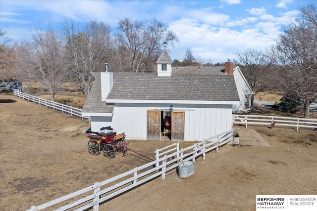 exterior space featuring an outbuilding, a barn, fence, roof with shingles, and a chimney