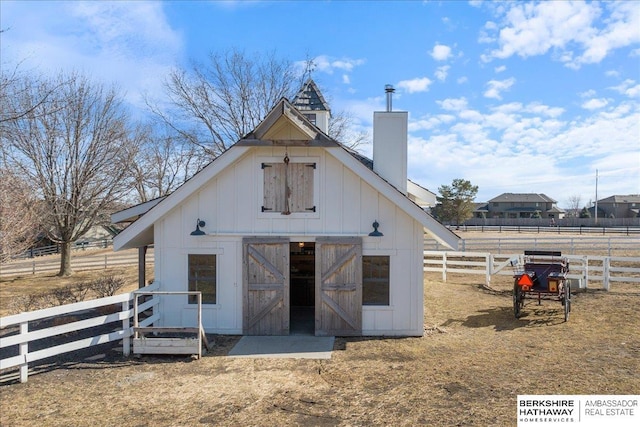 back of house with board and batten siding, a chimney, an outdoor structure, and fence