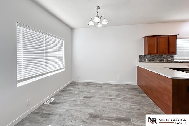 unfurnished dining area with light wood-style floors, visible vents, baseboards, and an inviting chandelier