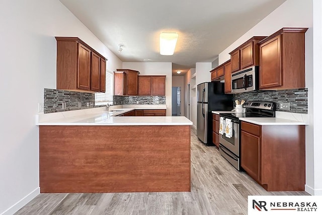 kitchen with decorative backsplash, appliances with stainless steel finishes, a peninsula, light countertops, and light wood-type flooring