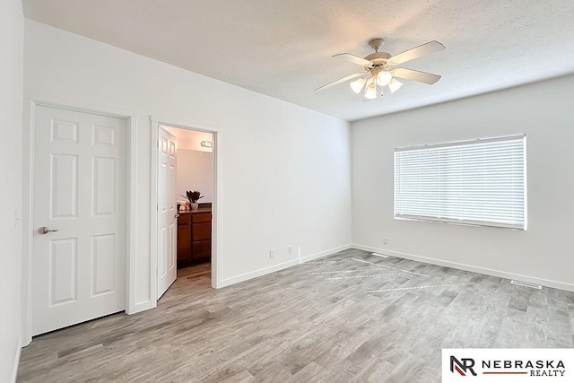 unfurnished bedroom featuring a textured ceiling, light wood finished floors, ensuite bath, and baseboards