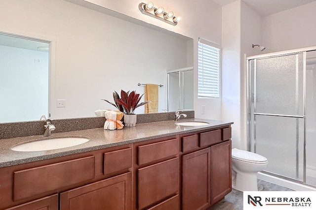 full bath featuring double vanity, a stall shower, a sink, and toilet