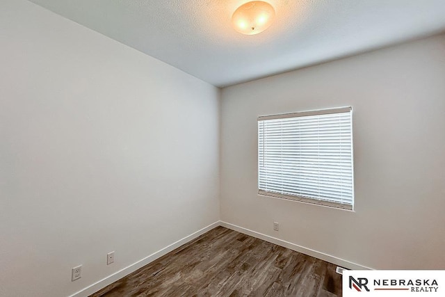 empty room featuring a textured ceiling, dark wood finished floors, and baseboards