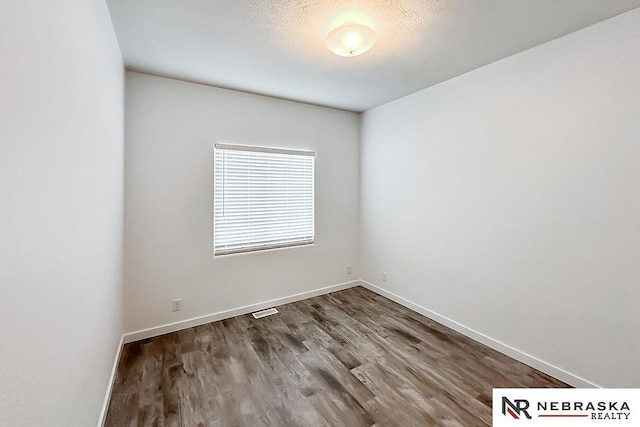 unfurnished room with a textured ceiling, wood finished floors, visible vents, and baseboards