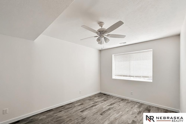 spare room with a textured ceiling, wood finished floors, visible vents, a ceiling fan, and baseboards