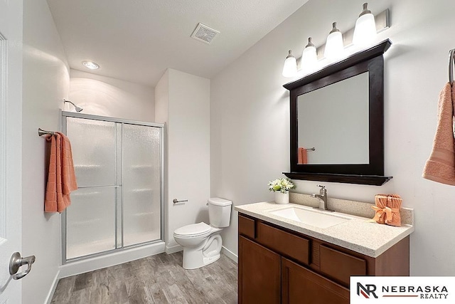 full bath featuring a stall shower, visible vents, toilet, wood finished floors, and vanity