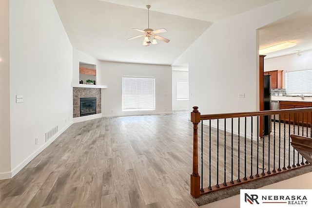 living room with light wood finished floors, visible vents, lofted ceiling, ceiling fan, and a fireplace