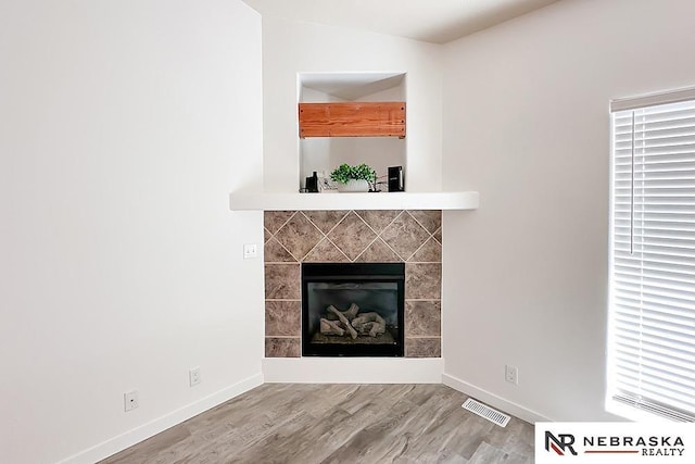 unfurnished living room with baseboards, visible vents, wood finished floors, and a tile fireplace