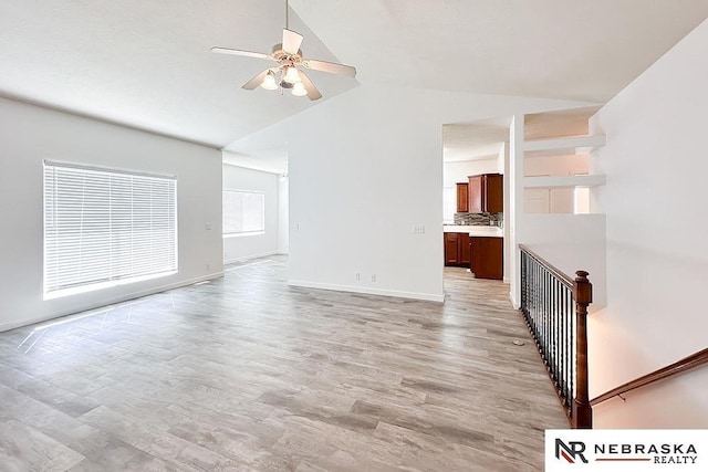 unfurnished living room featuring lofted ceiling, light wood-type flooring, baseboards, and a ceiling fan