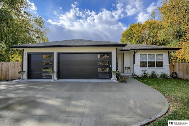 prairie-style home with stucco siding, concrete driveway, an attached garage, fence, and a front lawn