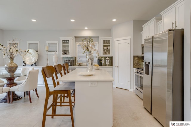 kitchen with tasteful backsplash, light countertops, appliances with stainless steel finishes, glass insert cabinets, and white cabinets