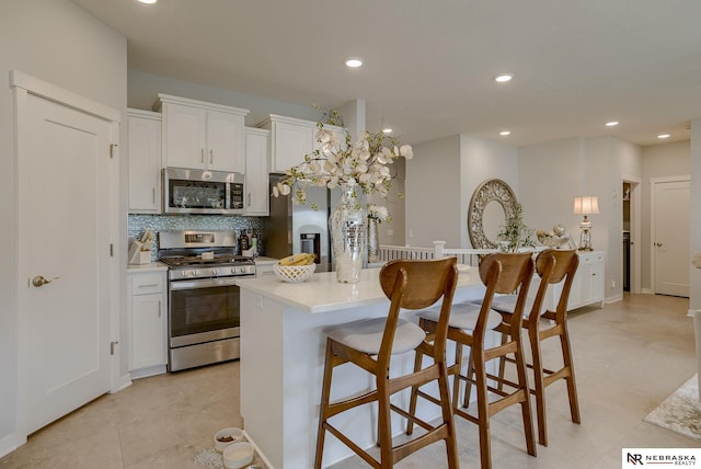 kitchen featuring a breakfast bar, a center island, decorative backsplash, appliances with stainless steel finishes, and white cabinets