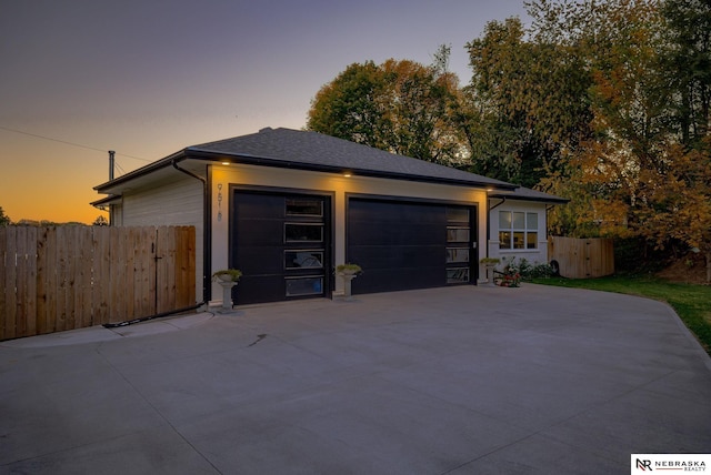 garage at dusk with concrete driveway and fence